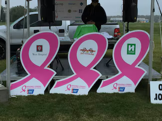 Three large pink ribbon signs with sponsor logos for the 