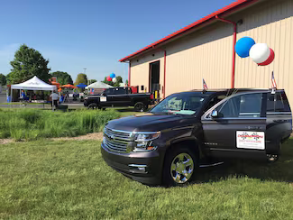 Front of a dark gray SUV with red, white, and blue balloons, and an open driver's side door, parked on grass.
